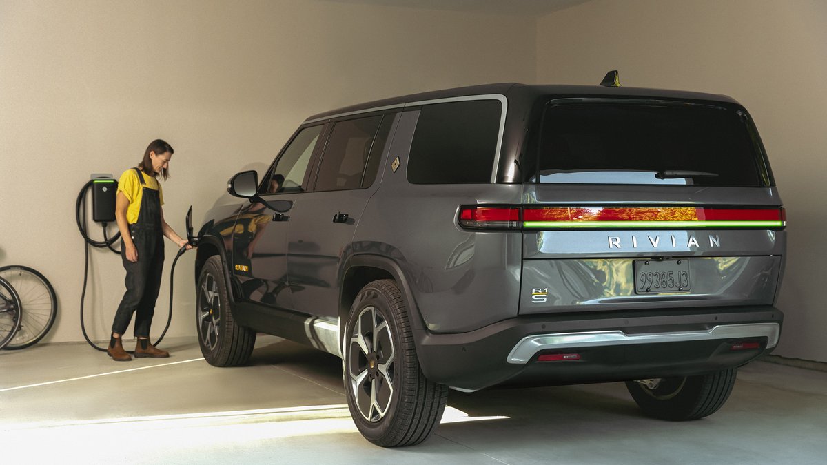 A 2025 Gray Rivian SUV is parked in a garage, being charged, with a bicycle hanging on the wall nearby.