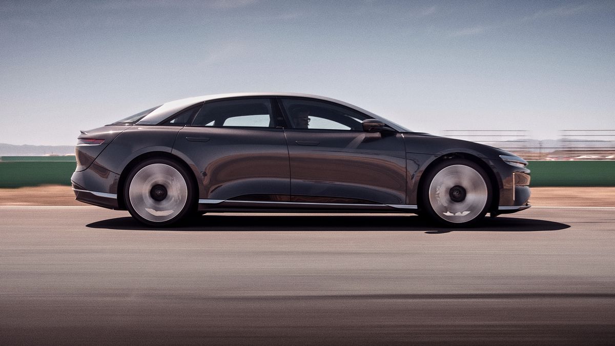 A 2025 Lucid Air GT sedan zooms past on a racetrack, showcasing its aerodynamic design and large alloy wheels against a blurred background.