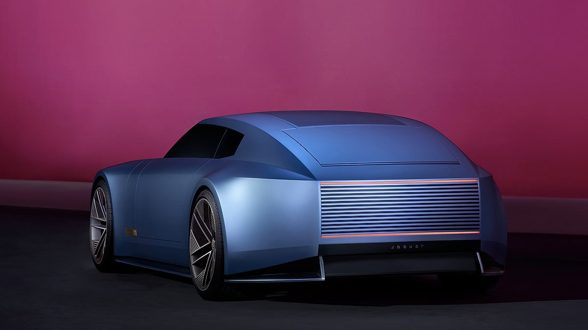 Blue Jaguar concept car shown from the rear in a studio setting with a magenta wall, dark floor, slim red taillights, and futuristic bodywork.