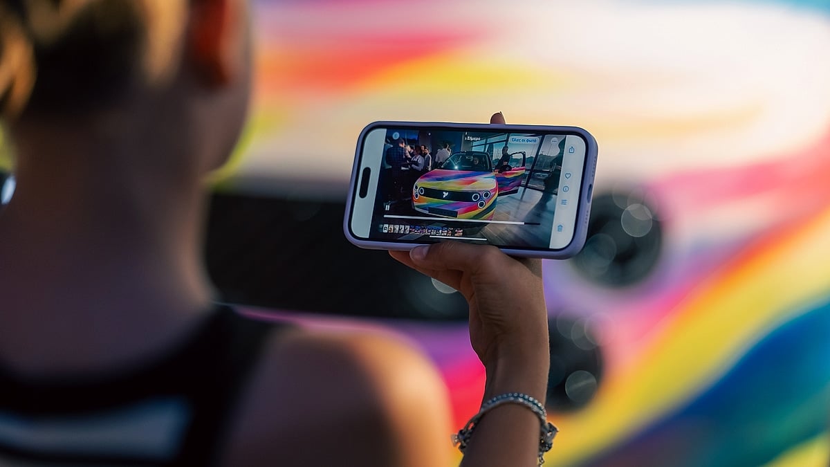A person holding a phone recording a colorful Firefly car.