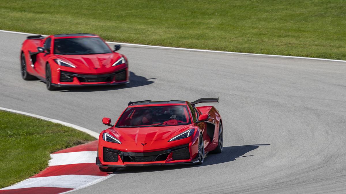 Two red Chevrolet Corvettes race on a curved track, showcasing their sleek design and speed in a dynamic environment.