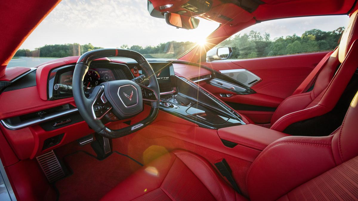 Interior of a red Corvette, featuring luxurious leather seats and high-tech dashboard, illuminated by a sunset glow.