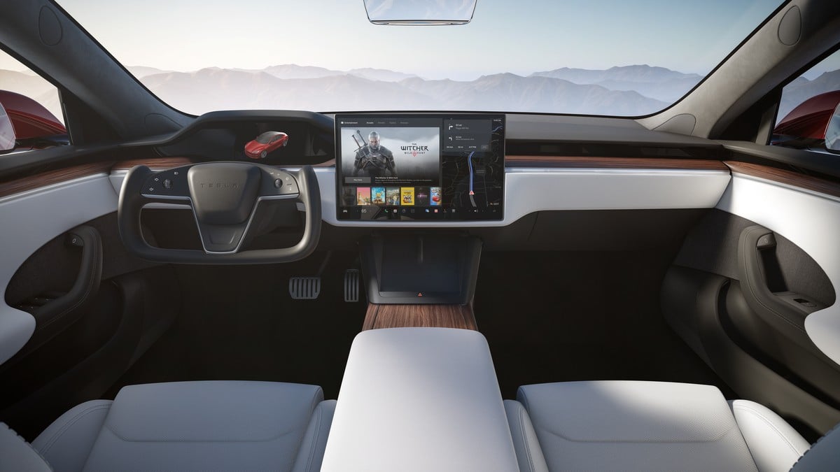 Interior view of a Tesla Model S Plaid with a modern dashboard, large touchscreen displaying games, and sleek white leather seats.