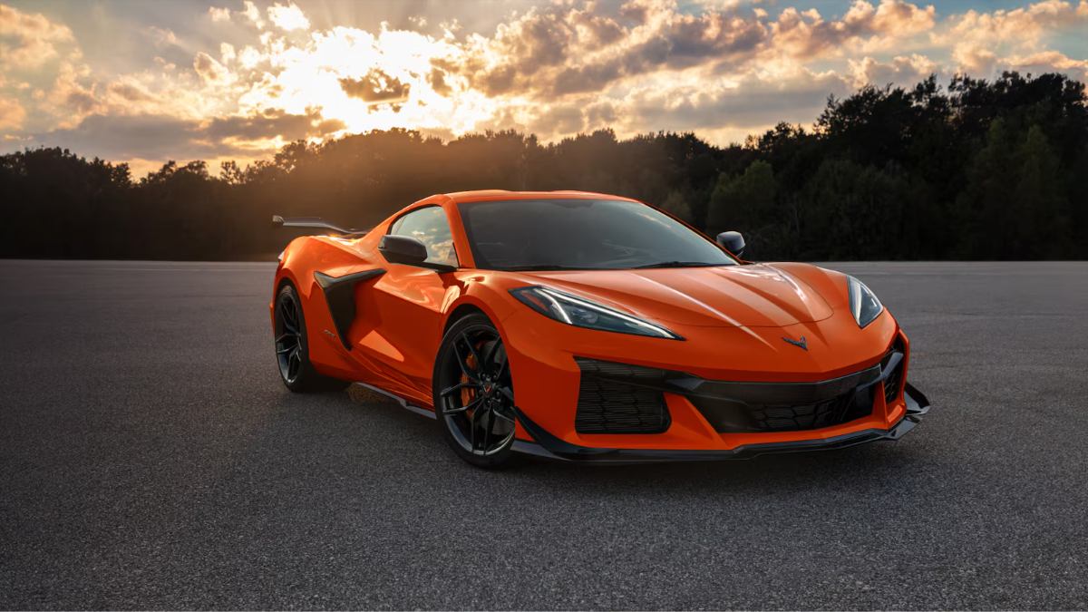 Bright orange 2025 Chevrolet Corvette Z06 with sleek lines, aggressive stance on asphalt with sunset and forest backdrop