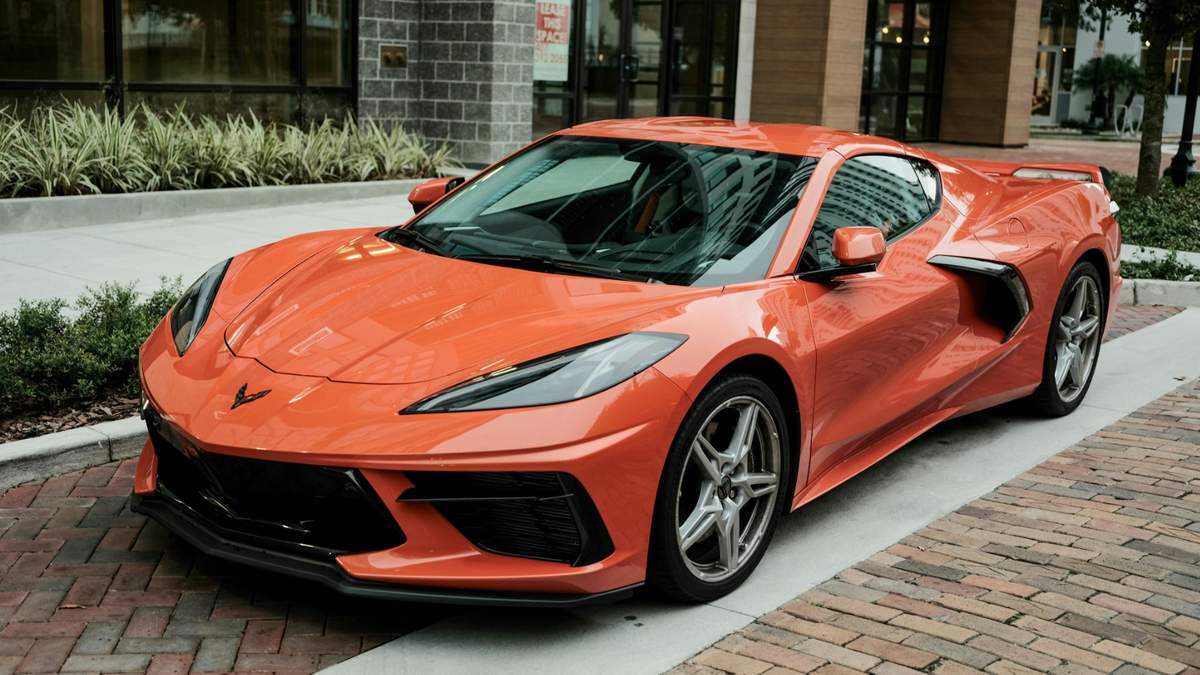 A 2025 orange Corvette C8 parked on a brick pathway, showcasing its modern design and sporty features in an urban setting.