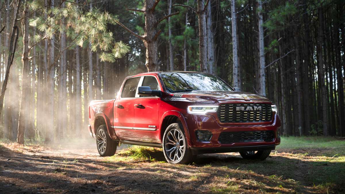 Red RAM 1500 pickup truck parked in sunlit pine forest with dust and light rays around rugged off-road wheels
