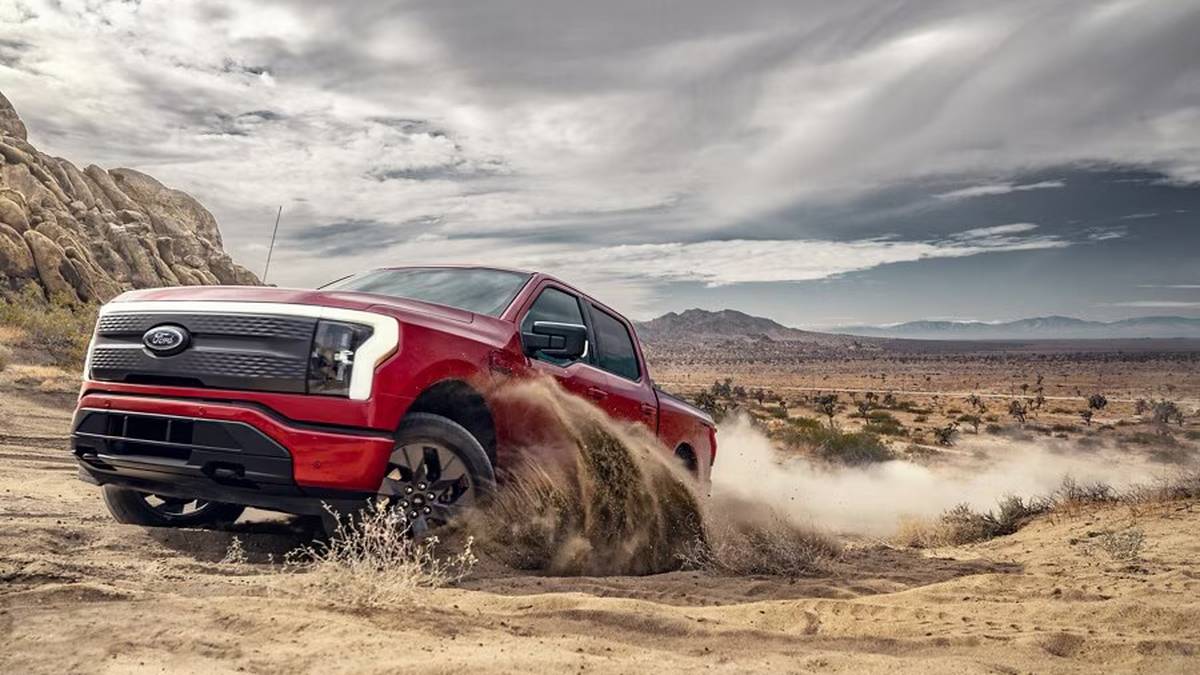 A red Ford truck kicking up dust while off-roading in a rocky, desert landscape under a cloudy sky.