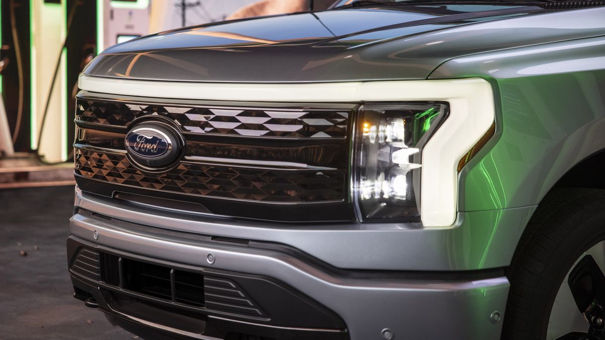Close-up of a silver 2025 Ford F-150 Lightning electric truck's front grille, featuring a distinctive logo and modern LED headlights.