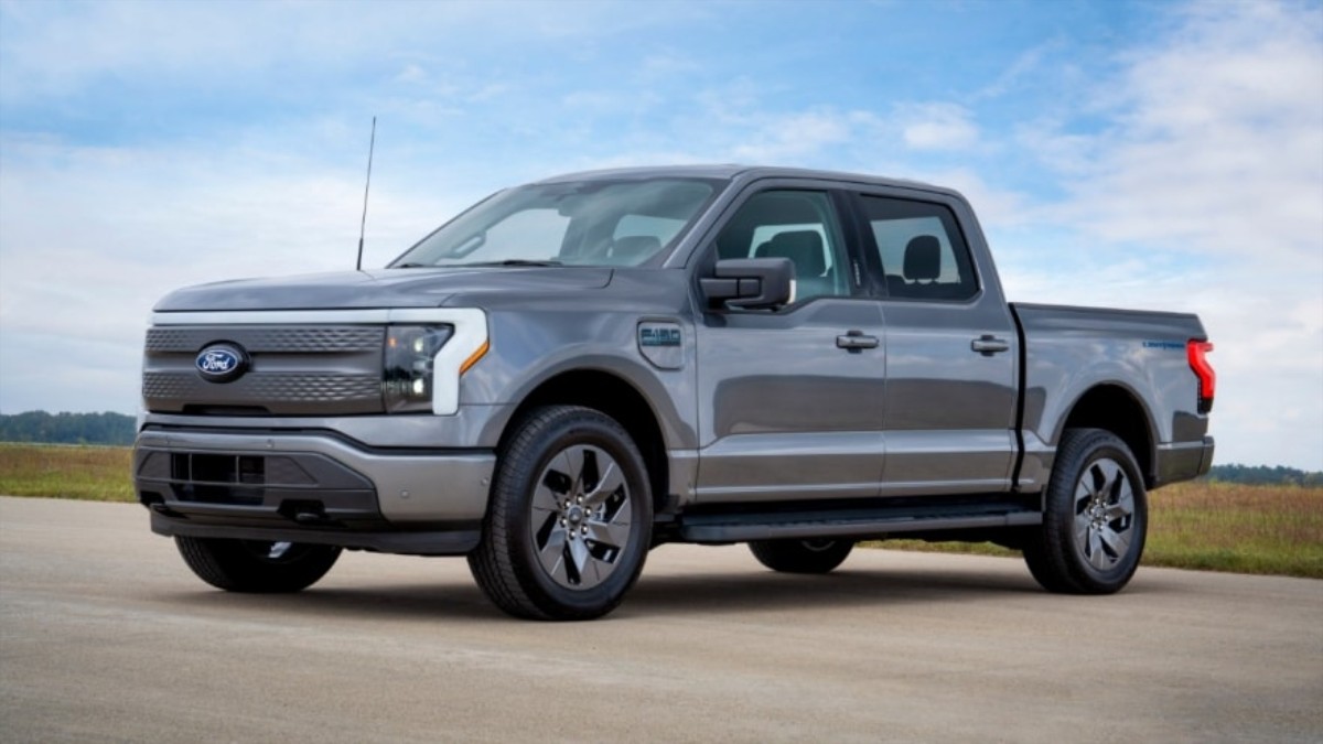 Silver Ford F-150 Lightning electric pickup truck parked on concrete with grassy field and blue sky background
