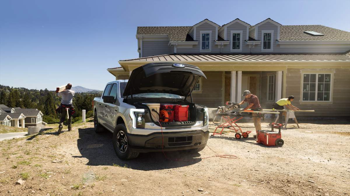 Silver 2025 Ford F-150 Lightning electric truck parked at construction site, frunk open, with workers using power tools