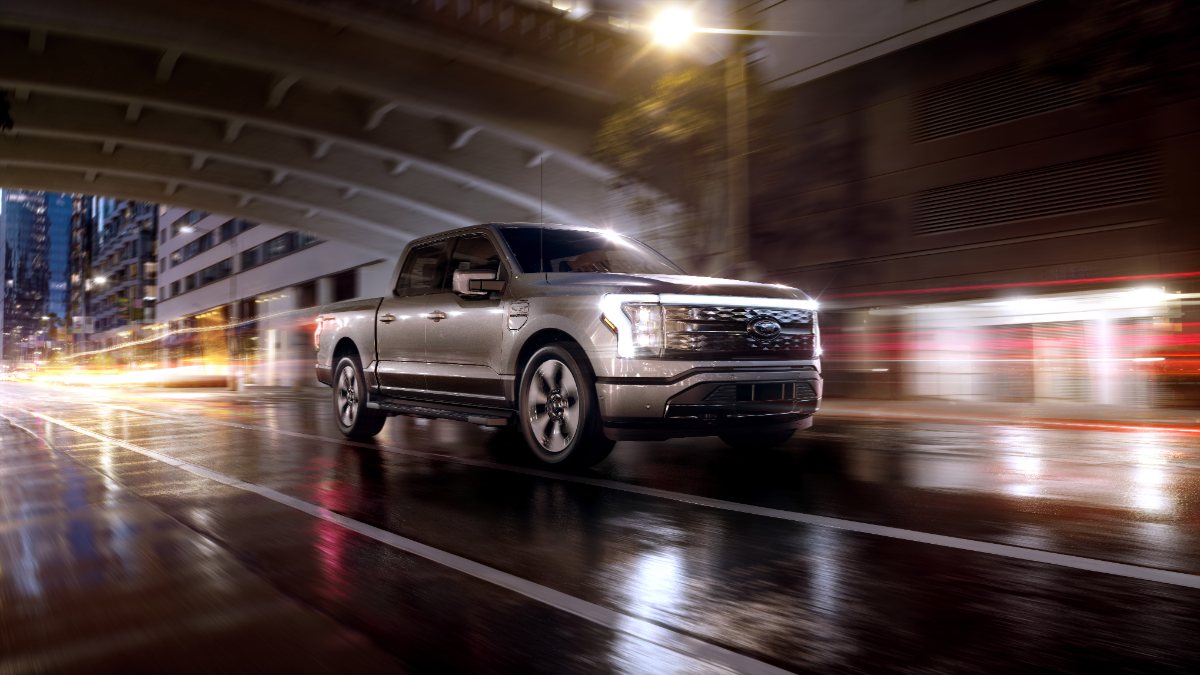 Silver Ford F-150 Lightning electric truck speeding on wet city street with motion blur and dramatic lighting at night