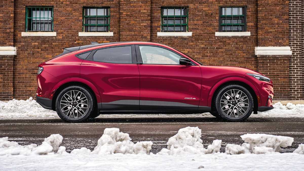 Deep red SUV parked on snowy street, sleek profile against rustic brick wall with intricate windows