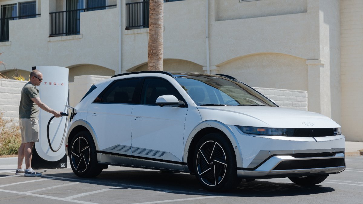 White Hyundai Ioniq 5 electric SUV charging at Tesla station, sleek angular design with black wheels