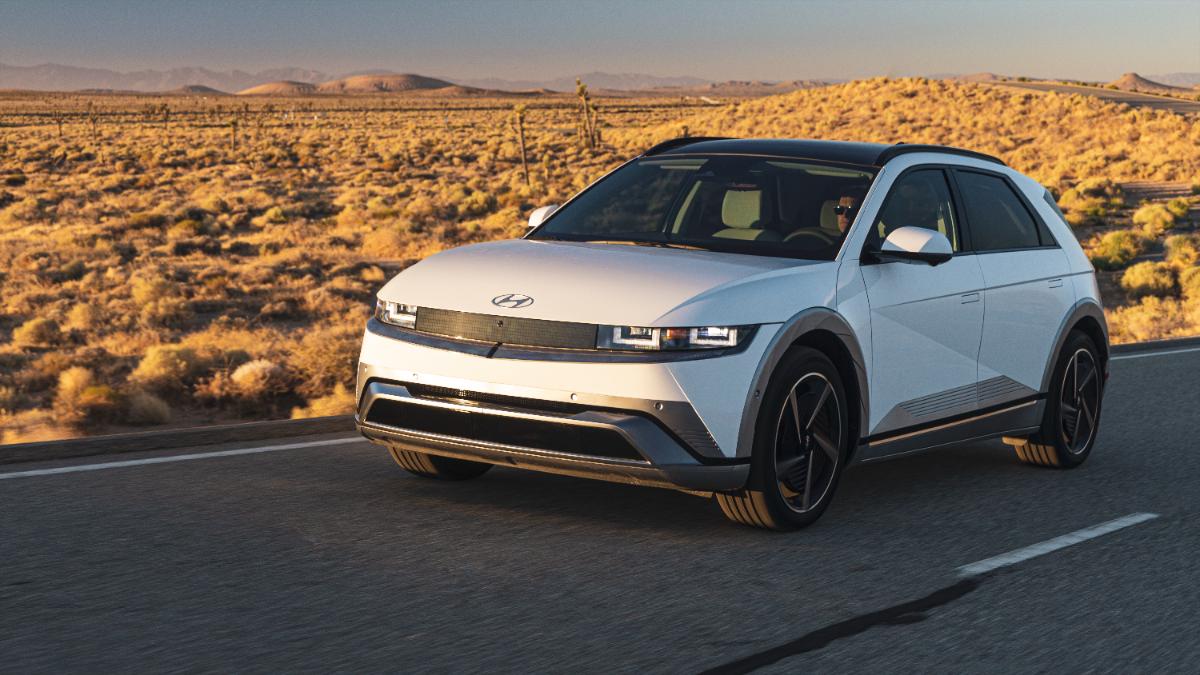 White Hyundai IONIQ 5 electric SUV driving on desert highway at sunset with golden landscape
