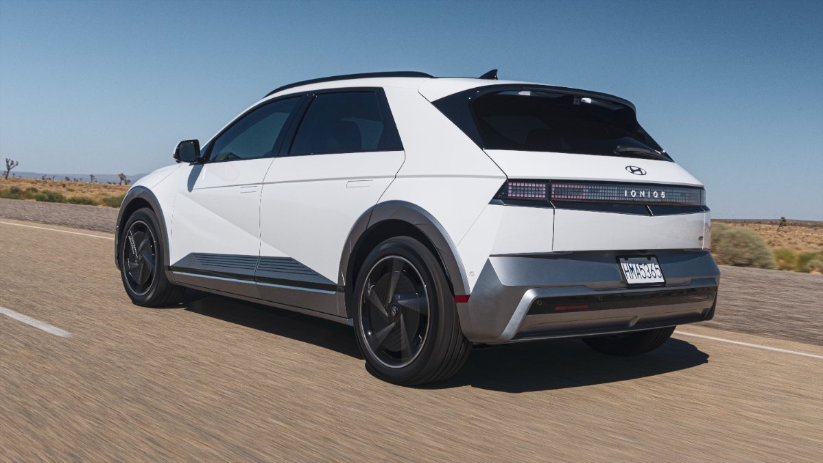 White 2025 Hyundai Ioniq 5 SUV with black trim driving on desert highway, angular design with pixelated taillights