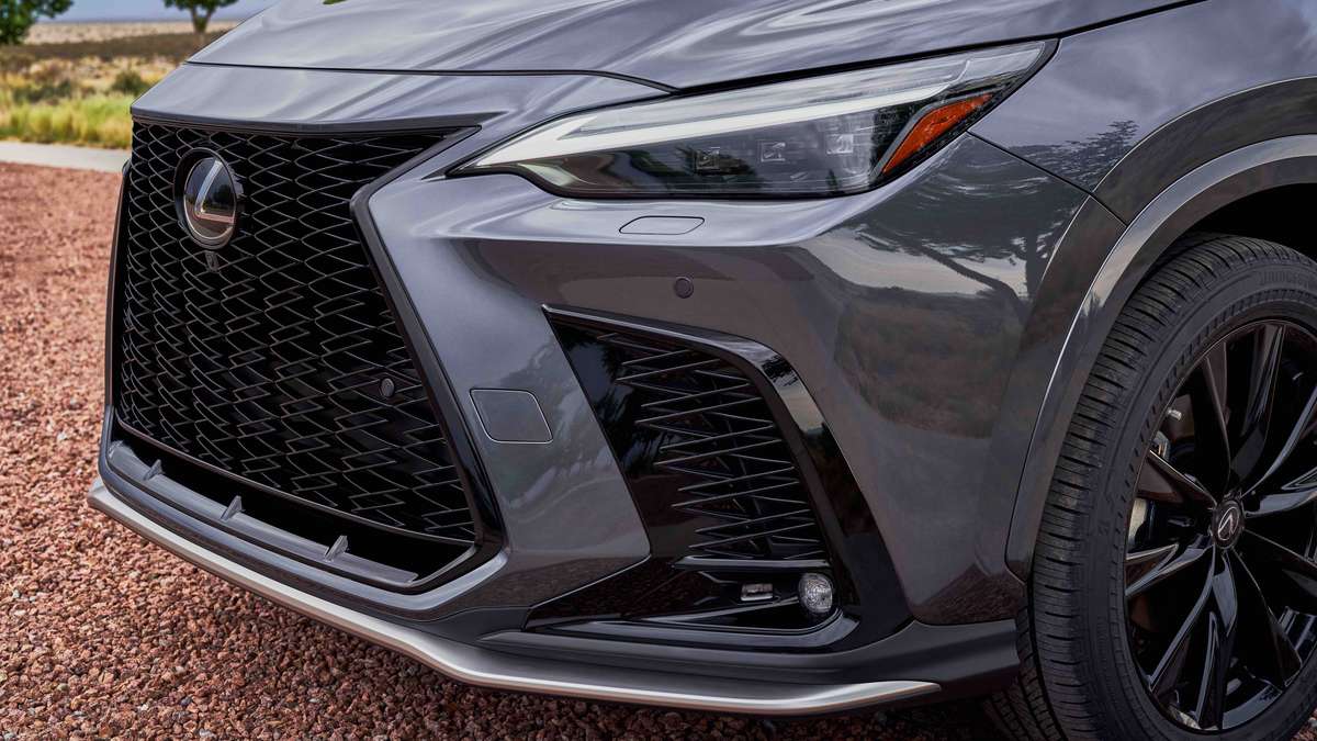 Close-up of a sleek gray Lexus SUV showcasing its bold front grille, stylish headlights, and modern design elements on gravel surface.