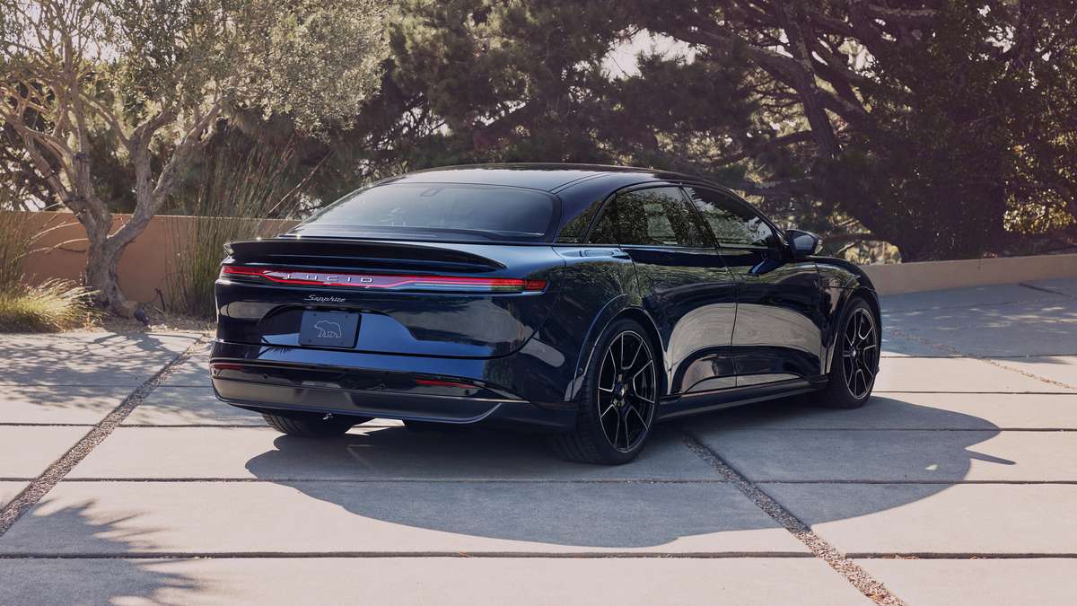 A sleek blue Lucid Air Sapphire parked on a driveway, surrounded by greenery, showcasing its modern design and sporty wheels.