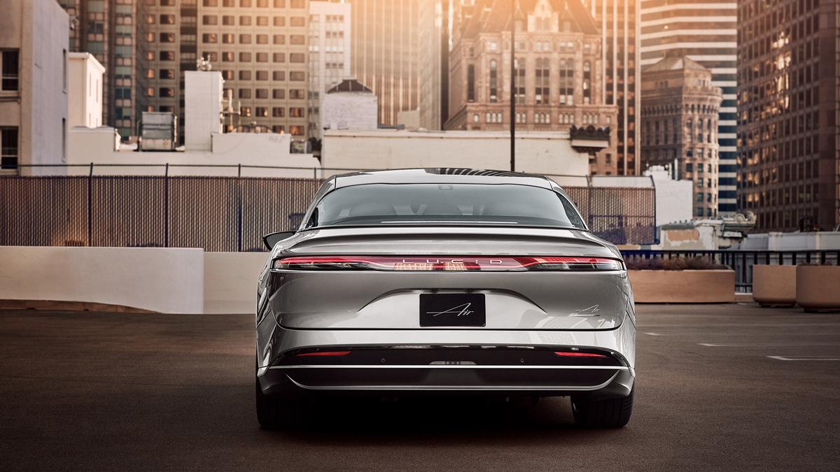 A silver 2025 Lucid Air electric car parks on a rooftop with a city skyline in the background, bathed in warm sunset light.