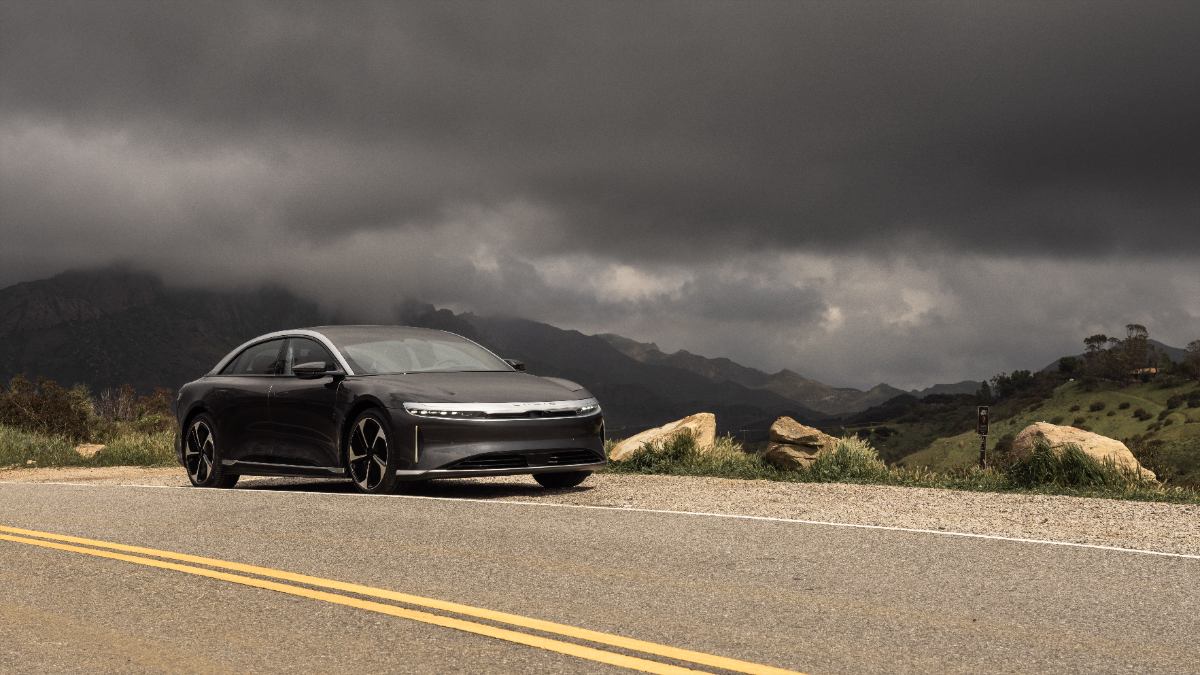 Black electric sedan parked on mountain road with dramatic stormy sky and rocky landscape background