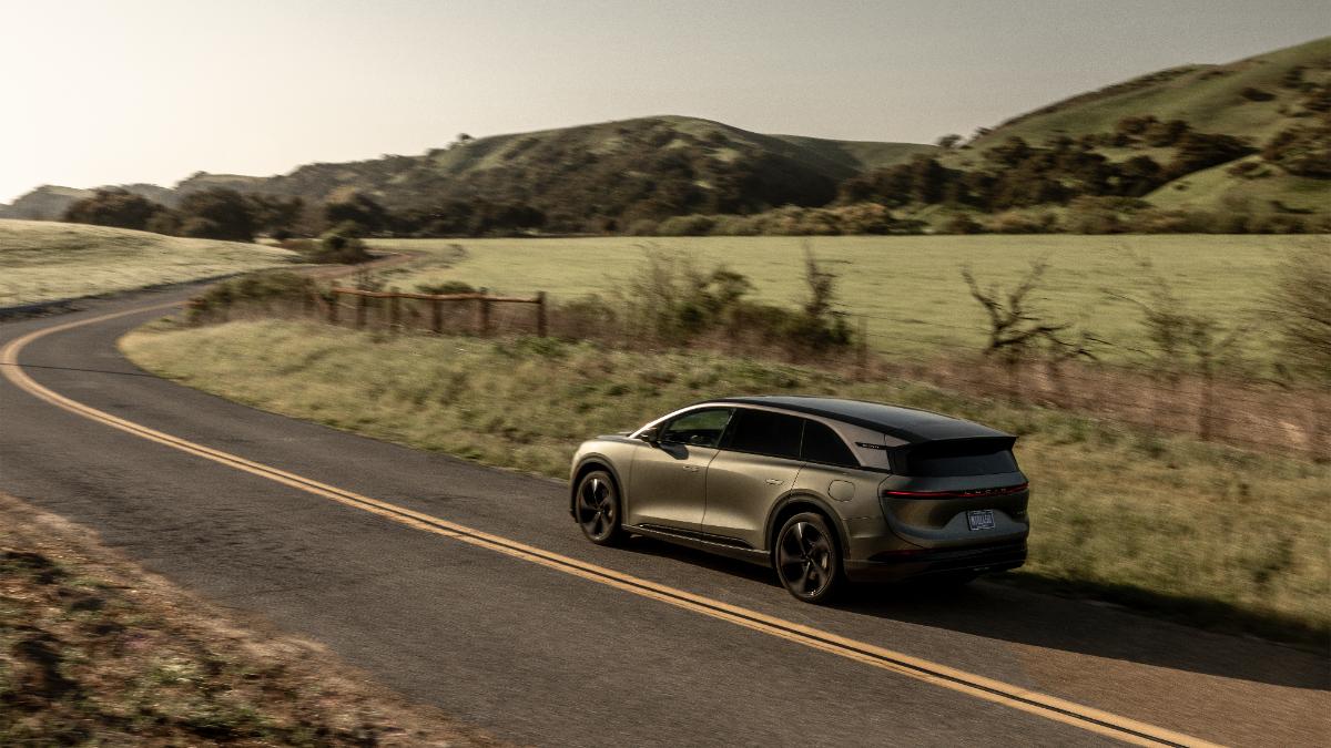 Sleek electric SUV driving on winding rural road through green rolling hills at sunset