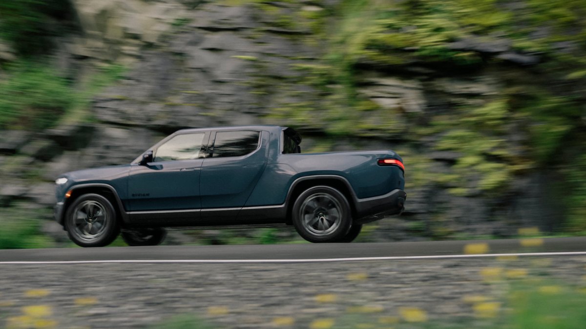 Dark blue electric pickup truck driving on mountain road with blurred rocky background