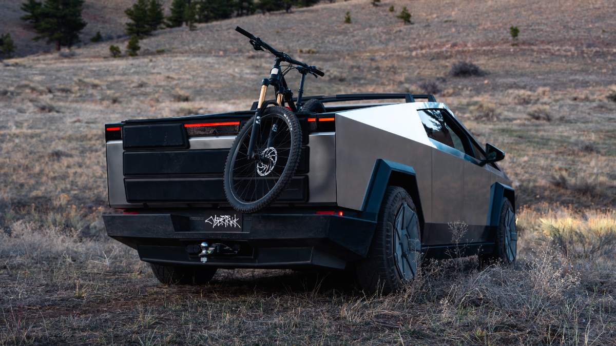 2025 Tesla Cybertruck in metallic silver, rear view with mountain bike mounted, parked on rugged desert terrain
