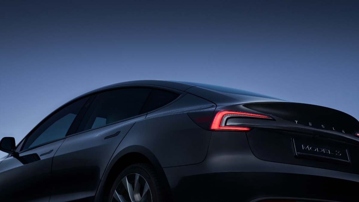 Black Tesla Model 3 at dusk, rear quarter view with glowing red taillight against dark blue sky