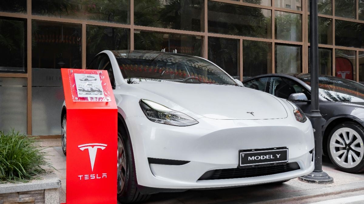 White 2025 Tesla Model Y parked near glass building, red Tesla display stand highlighting electric SUV design