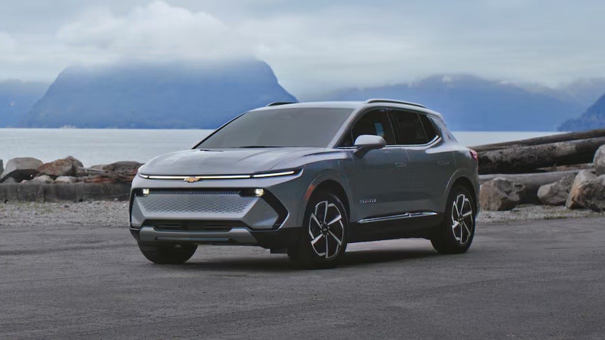 Alt text: 2025 Chevrolet Equinox EV in gray displayed at front three-quarter angle with ocean view in the background.
