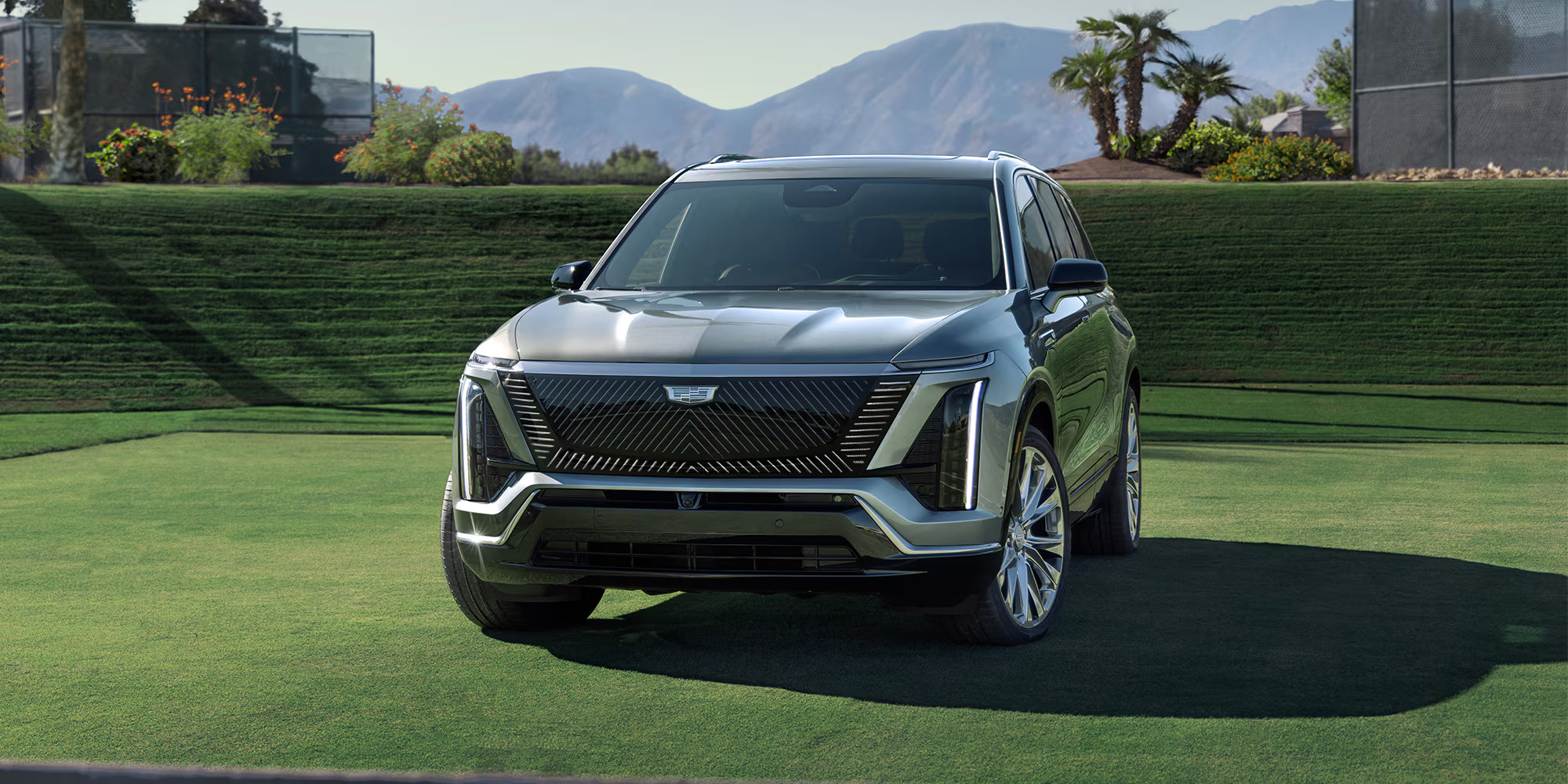 A sleek gray 2026 Cadillac Vistiq parked on a manicured lawn with mountains in the background, highlighting its modern design.