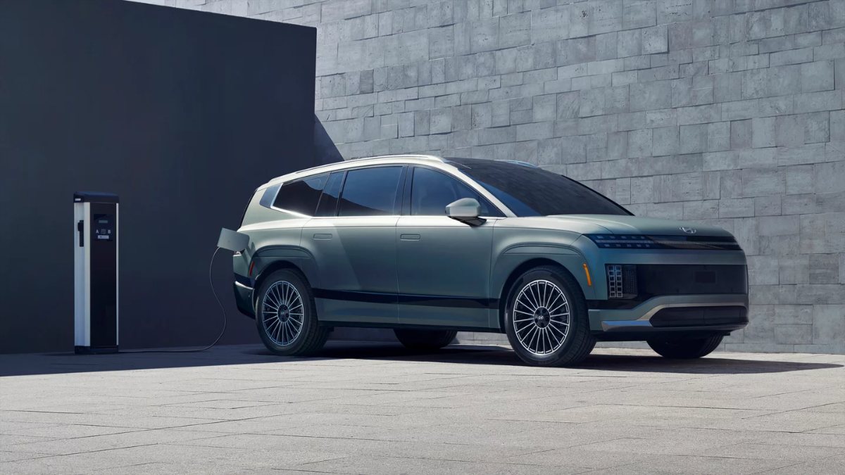 2026 Hyundai Ioniq 9 electric SUV in sage green, parked beside charging station with geometric concrete wall background