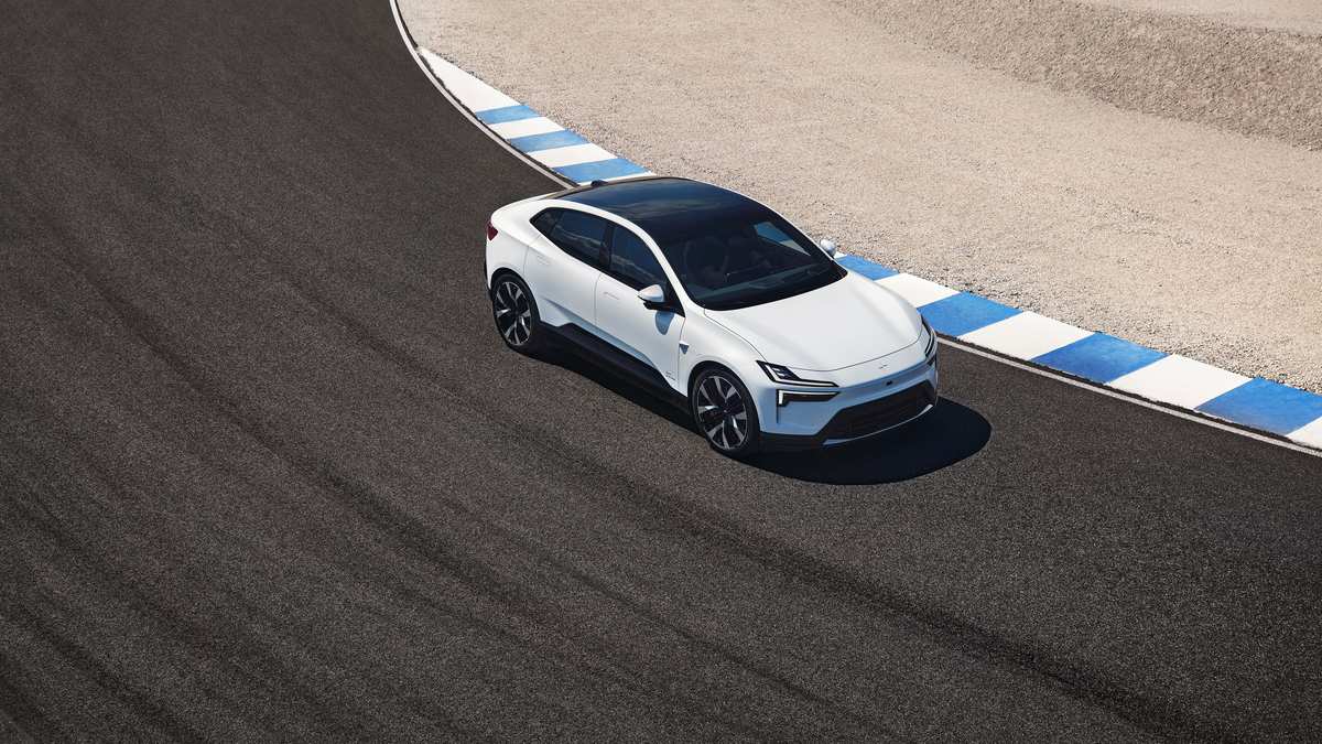 A sleek white sedan with a black roof navigates an asphalt racetrack, showcasing its sporty design against a blue-and-white striped barrier.