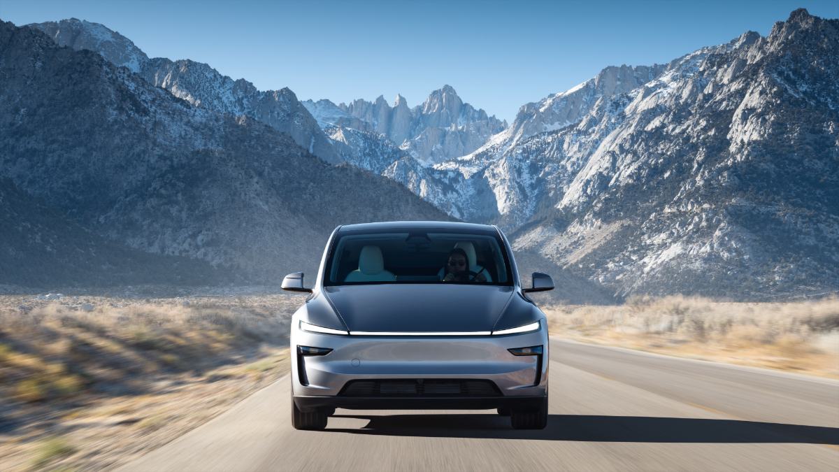 Silver electric SUV driving on mountain road with snow-capped Sierra Nevada peaks in background, sleek modern design