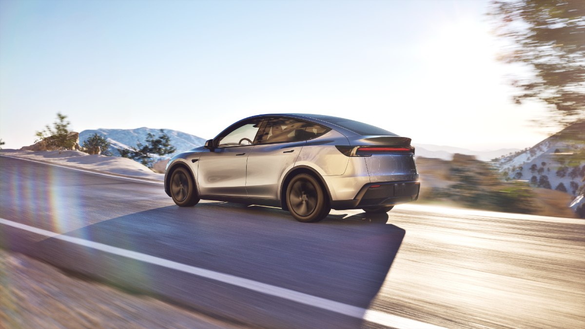 Silver 2026 Tesla Model Y Juniper driving on mountain road with blurred motion and snowy landscape