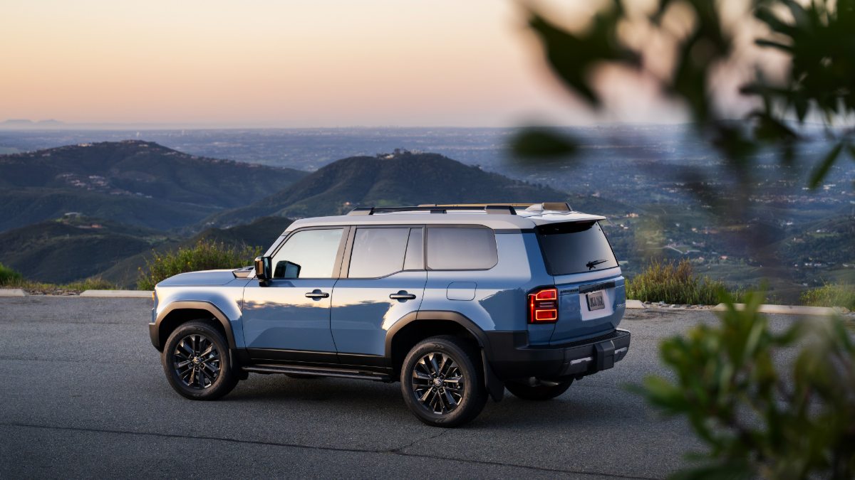Blue SUV parked on a scenic mountain road overlooking a vast valley at sunset.