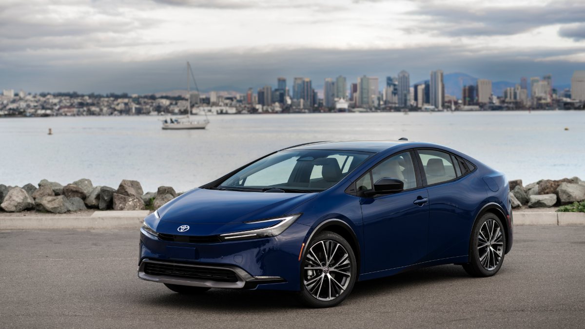 Navy blue Toyota Prius parked along waterfront with city skyline and sailboat in background