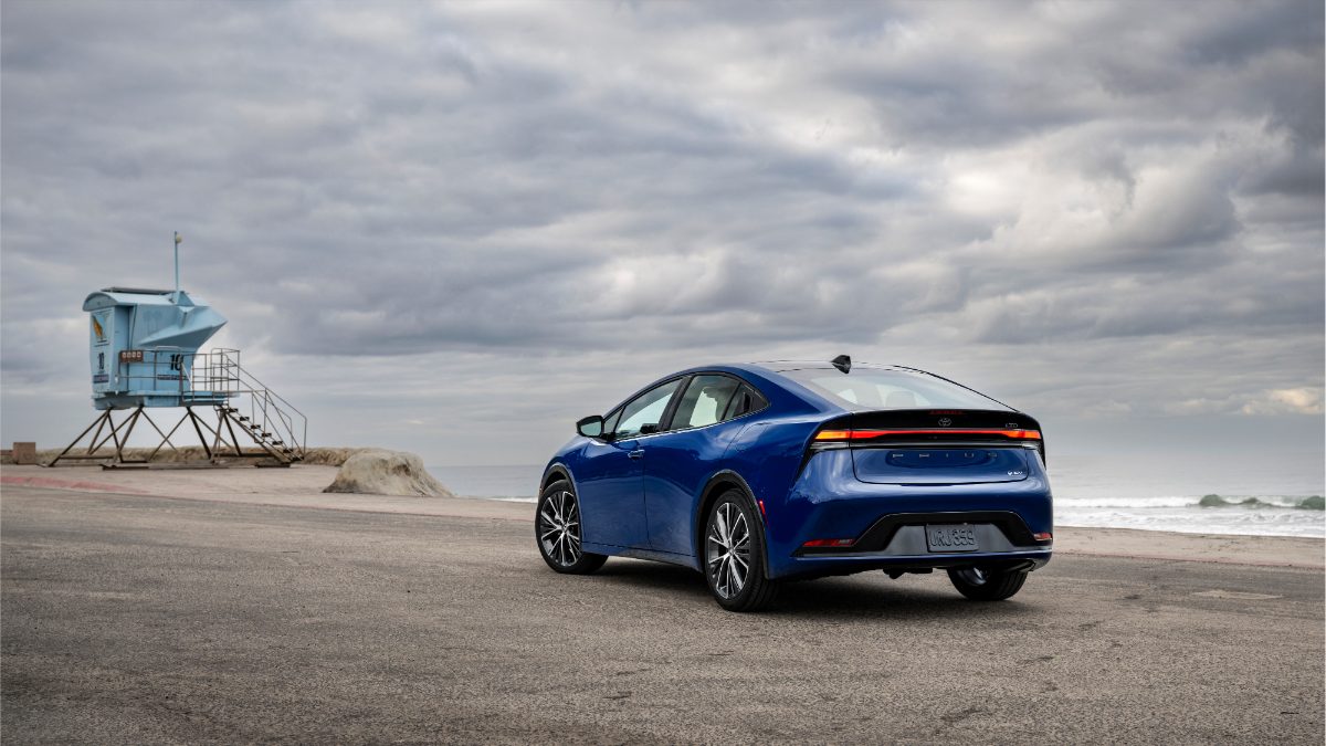 A blue car parked on a coastal road, beside a lifeguard tower, under a cloudy sky with ocean waves in the background.