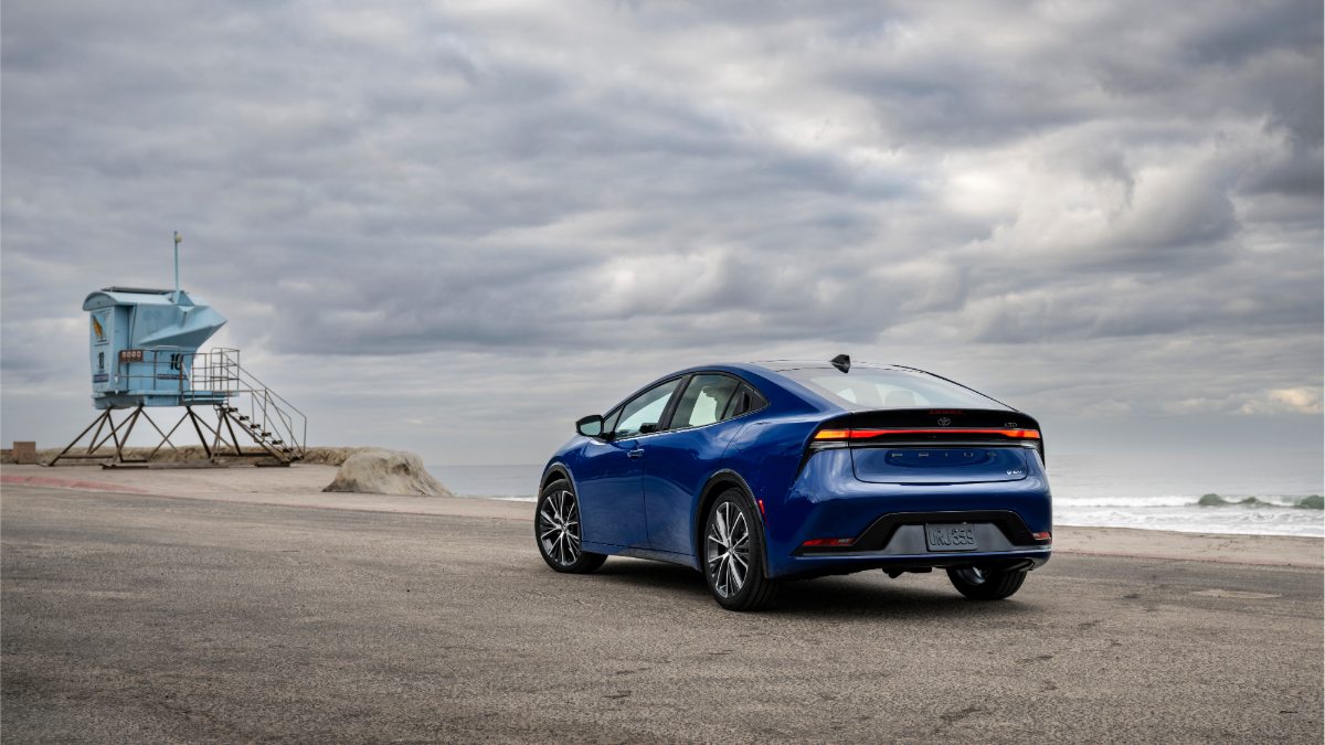 Blue Toyota Prius parked on beach near lifeguard tower under cloudy coastal sky