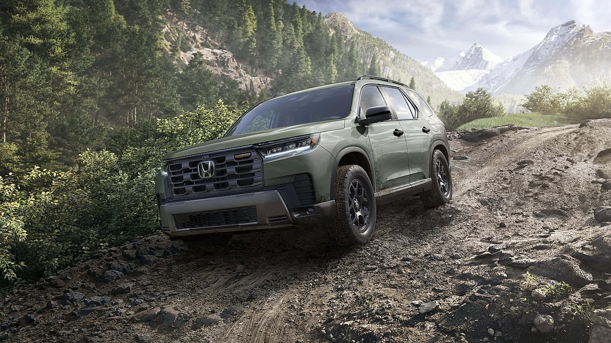 2026 Honda Pilot TrailSport climbing a rocky mountain trail surrounded by forest and snow-capped peaks.