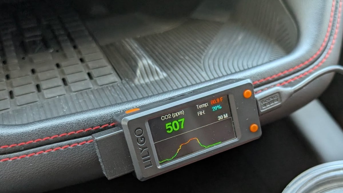 Digital CO2 monitor displaying 507 ppm, 80.9°F temperature, and 29% humidity, placed in a vehicle's interior with red stitching.