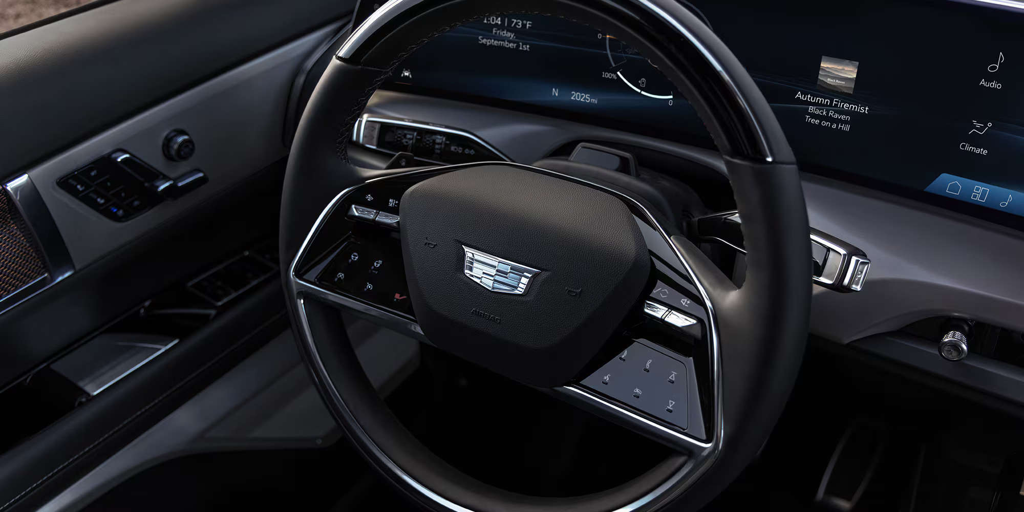 Close-up of a 2026 Cadillac Vistiq steering wheel featuring a sleek design, dashboard display with date and music info, and modern controls.