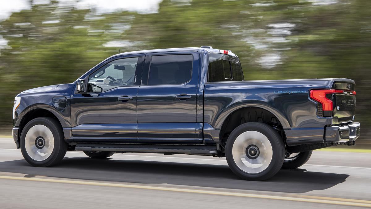 A blue Ford F-150 Lightning drives dynamically on a highway, showcasing its sleek design and modern features with blurred background.