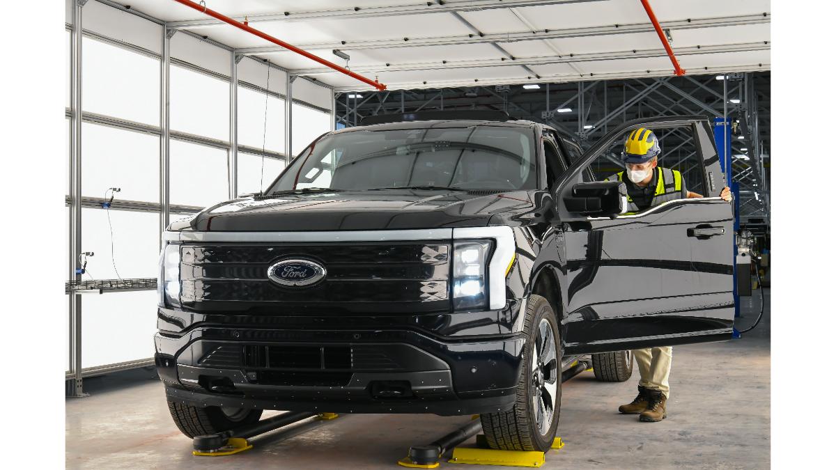 Ford F-150 Lightning electric truck driving through snowy forest with headlights illuminating snow-covered trees