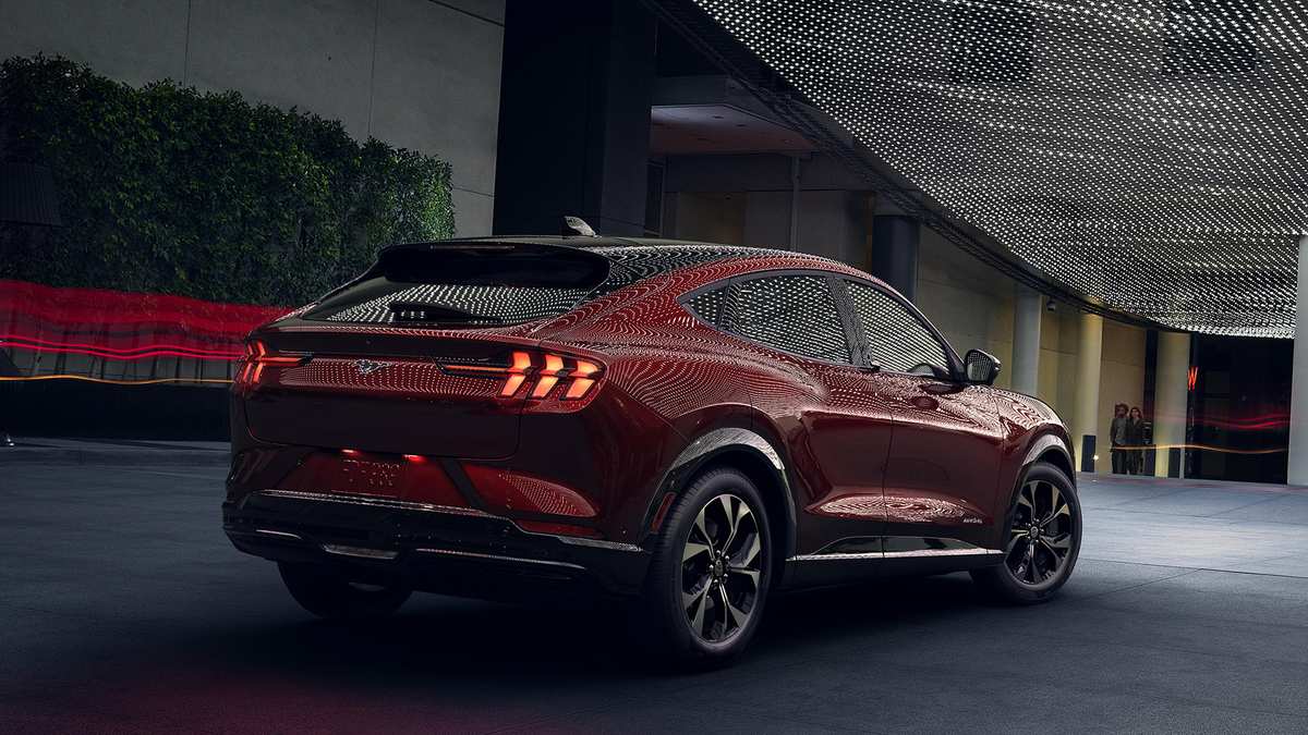 A sleek red electric SUV parked under a modern architectural canopy, showcasing its stylish design and glowing tail lights.