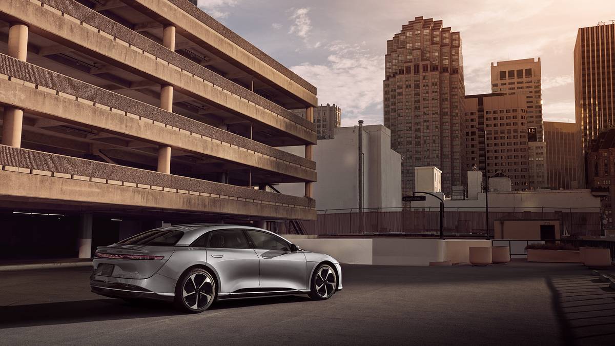 A Gray 2025 Lucid Air Touring parked on the rooftop of a city parking garage, skyscrapers silhouetted by a warm sunset.
