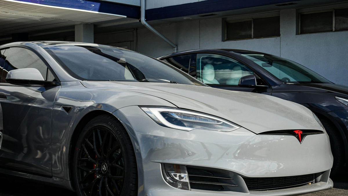 A silver Tesla Model S with black alloy wheels parked next to a dark gray vehicle in a modern setting.