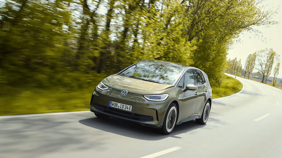 A sleek, olive-green Volkswagen ID.3 electric car speeding along a winding road surrounded by lush greenery.