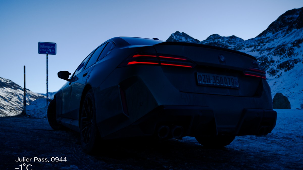 A Green 2025 BMW M5 parked near the snow-covered Julier Pass sign, with mountains in the background and a chilly temperature of -1°C.