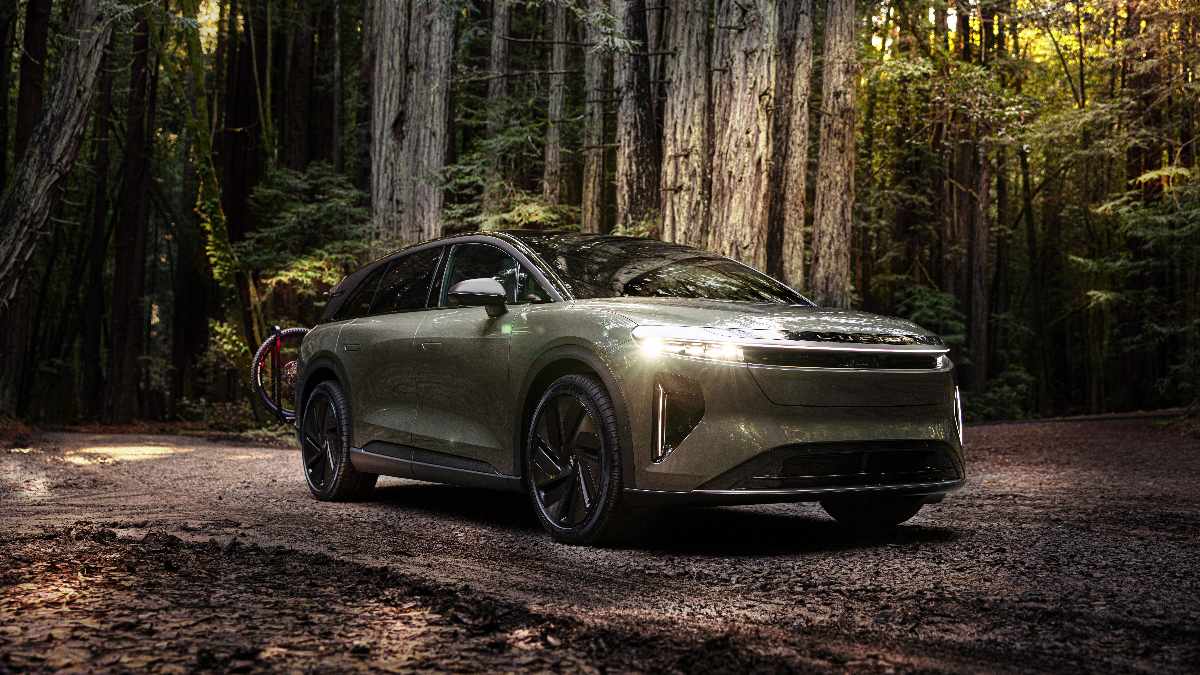 A sleek, Lucid Gravity parked on a dirt path surrounded by towering green trees in a serene forest setting.