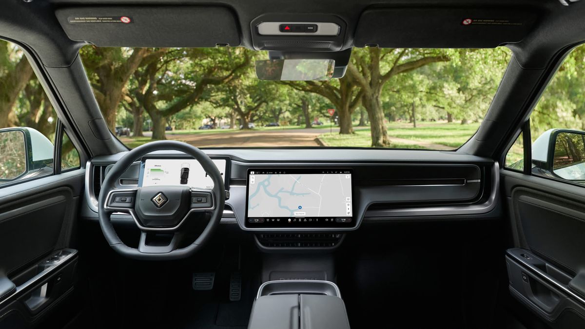 Interior view of a 2025 Rivian R1S with large touchscreen displays, surrounded by natural greenery.